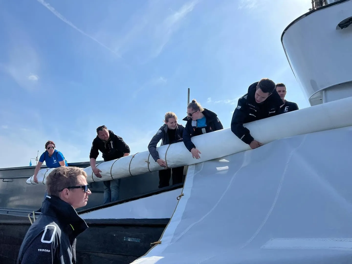 Bemanningsleden tillen samen een opgerold zeil aan boord.